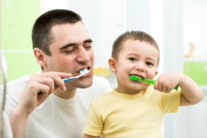 A father with his young son teaching him how to brush his teeth
