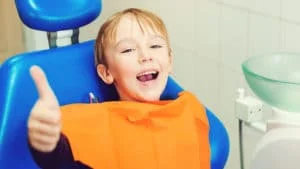 A young boy giving a thumbs up during his first dental visit. 